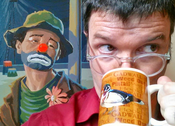 Blogger with coffee mug and sad clown painting