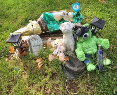 grave with teddy bears, solar lights, and deflated champagne bottle balloon