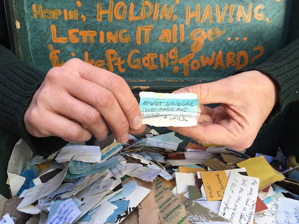 Hands holding scrap of paper with the writing "Regret drug life that made me loose a child" (sic.)
