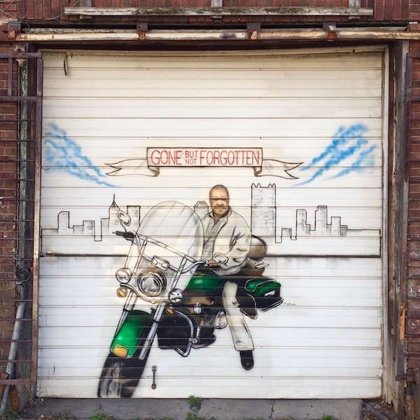 Mural painted on garage door of man on motorcycle with the Pittsburgh skyline behind him and a banner reading "Gone but not Forgotten"