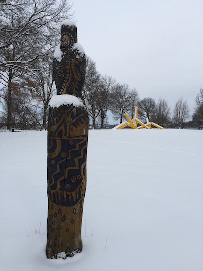 Wooden Persephone Project sculpture in snow with John Raymond Henry "Pittsburgh" (aka "The French Fry sculpture") in background, Frank Curto Park, Pittsburgh, PA