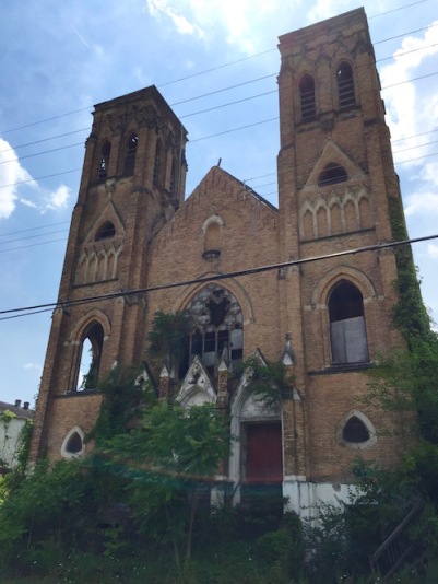 exterior of former Holy Trinity Catholic church, Duquesne, PA missing windows and trees growing over front steps