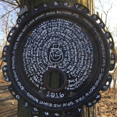 round metal lid painted with long string of text nailed to telephone pole, Pittsburgh, PA