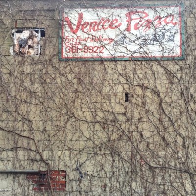 hand-painted sign for Venice Pizza on cinderblock wall, covered in vines, Pittsburgh, PA