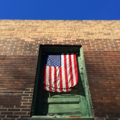 American flag hanging in second-floor doorway of brick house, Pittsburgh, PA
