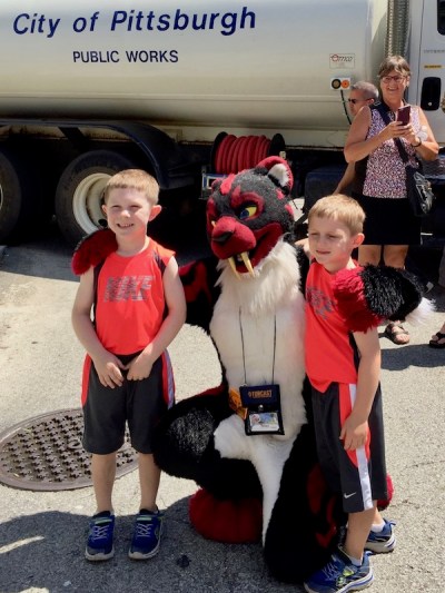 two children posing for photograph with person in fursuit costume of sabretooth tiger at Anthrocon 2017 Fursuit Parade, Pittsburgh, PA