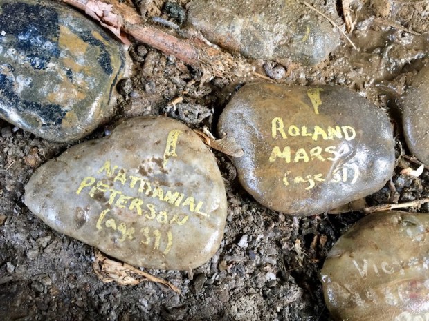 river stones painted with white text reading "Nathanial Peterson (age 39)" and "Roland Mars (age 31)", Pittsburgh, PA