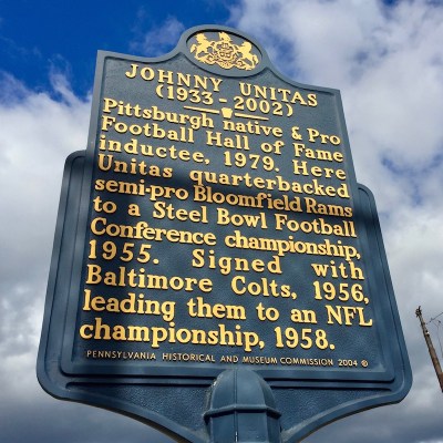 historical plaque honoring Johnny Unitas that reads "(1933-2002) Pittsburgh native & Pro Football Hall of Fame inductee, 1979. Here Unitas quarterbacked semi-pro Bloomfield Rams to a Steel Bowl Football Conference championship, 1955. Signed with Baltimore Colts, 1956, leading them to an NFL championship, 1958.