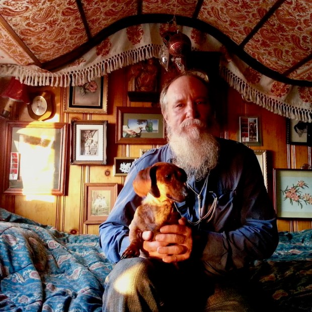 icon painter Simeon Larivonovoff sitting on a bed with a small dog on his knee