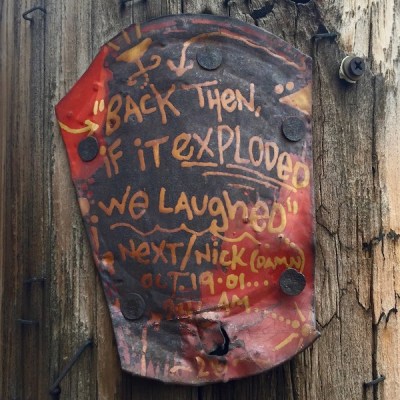 Cut tin can painted with text and nailed to telephone pole. Text reads "Back then, if it exploded, we laughed", Pittsburgh, PA