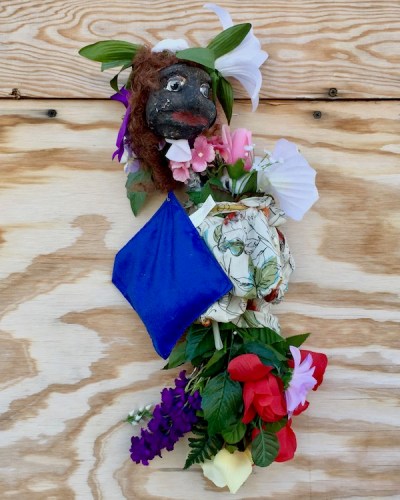 sculpture of black plaster head with flowers attached to wood