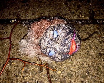 sculpture of black plaster head laying on wet sidewalk concrete