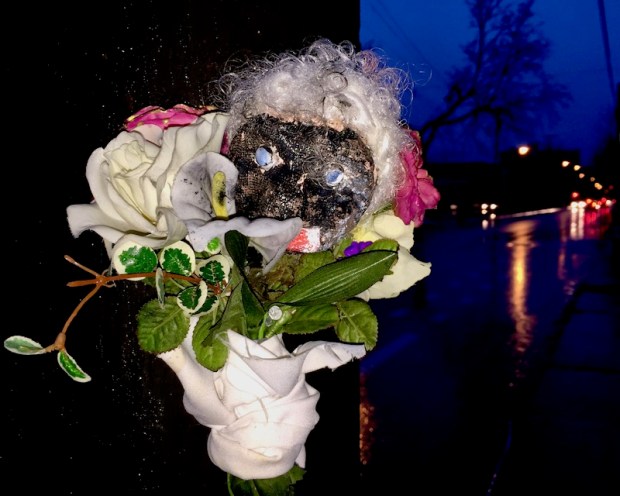 sculpture of black plaster head with fake white hair and flowers attached to utility pole