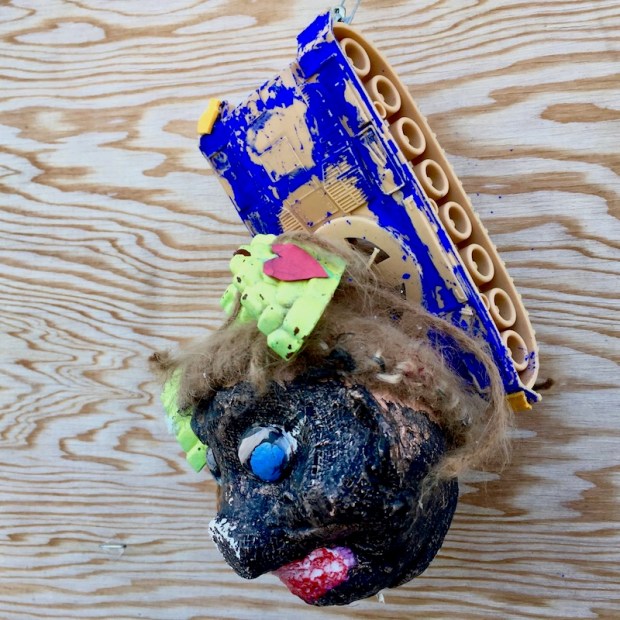 sculpture of black plaster head with plastic toy tank attached to wood