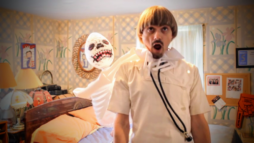 video still of Weird Paul dressed as a doctor with inflatable skeleton choking him
