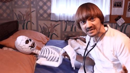 video still of Weird Paul dressed as a doctor with inflatable skeleton as patient