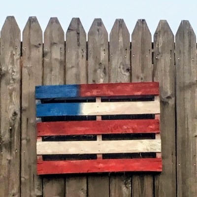shipping pallet painted like American flag hanging on wooden fence