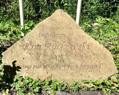 engraved stone with the text "In Memory of Kim Rutkowski, 2005, 'Always put your best foot forward'"