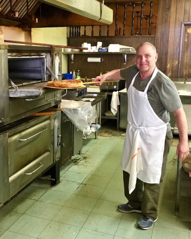 pizza chef pulling cooked pizza from oven