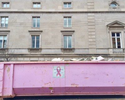 pink breast cancer awareness dumpster in front of large stone building