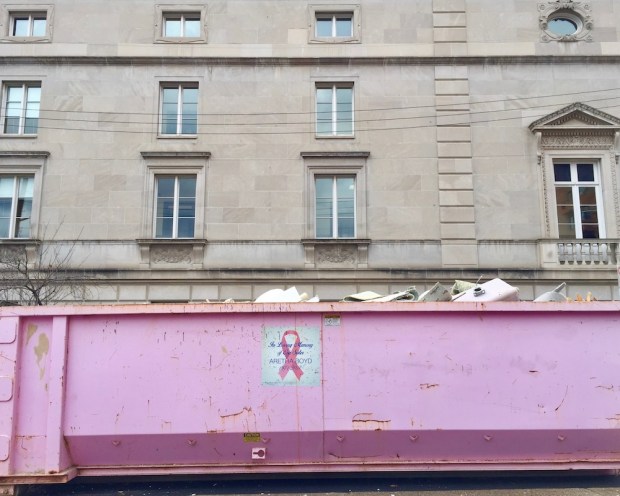 pink breast cancer awareness dumpster in front of large stone building