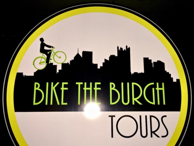 sign for Bike the Burgh Tours with a bicycle rider on a silhouette of the Pittsburgh skyline