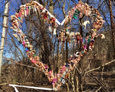 large number of Barbie dolls hung on a chain link fence in the shape of a heart
