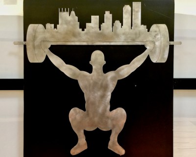 metal logo for Legends of Pittsburgh gym with weightlifter holding barbell with the city of Pittsburgh skyline on it