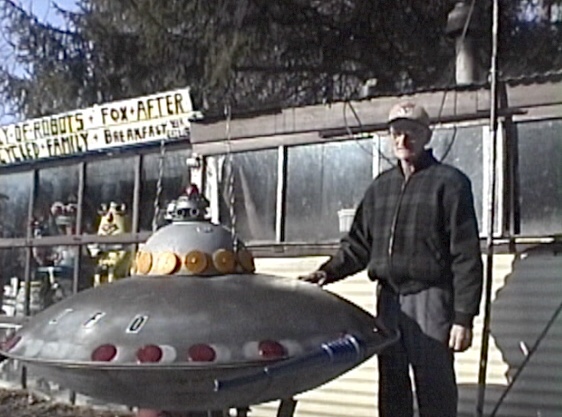 artist DeVon Smith with sculpture of UFO in front of his home in Wampum, PA, 2001