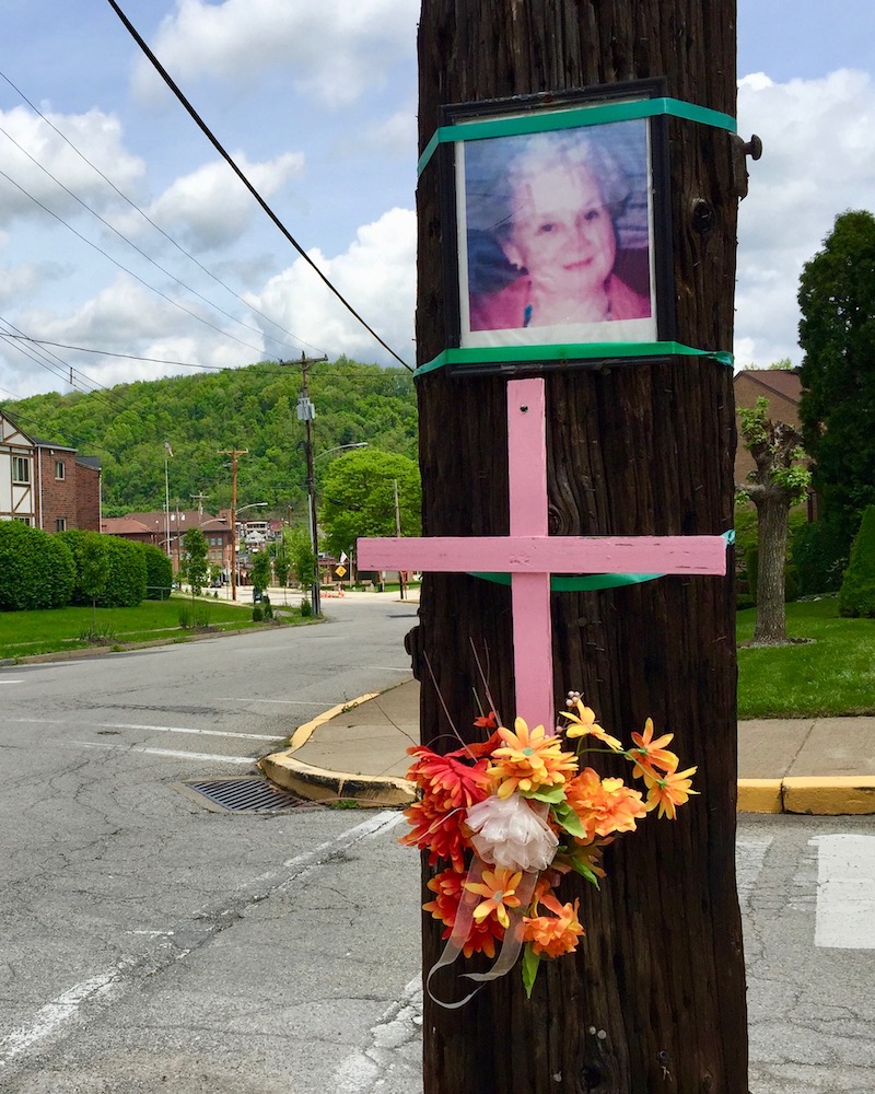 memorial featuring photograph, pink cross, and flowers on utility pole