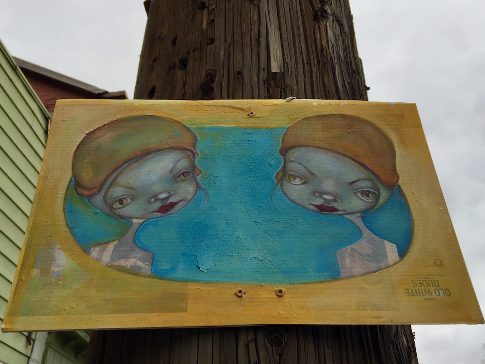painting of two girls with big eyes hung on utility pole