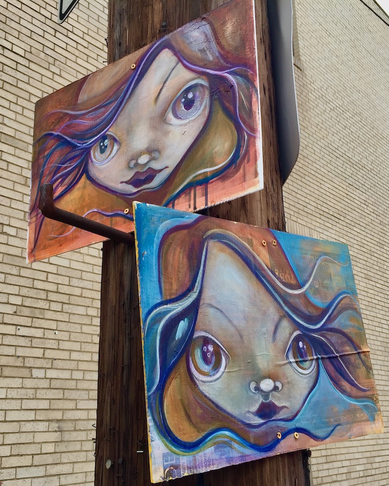 pair of paintings of girls with big eyes hung on utility pole