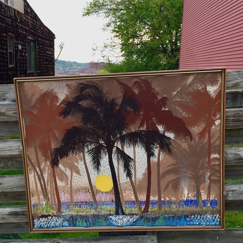 painting of palm trees and sunset over ocean hung on exterior fence