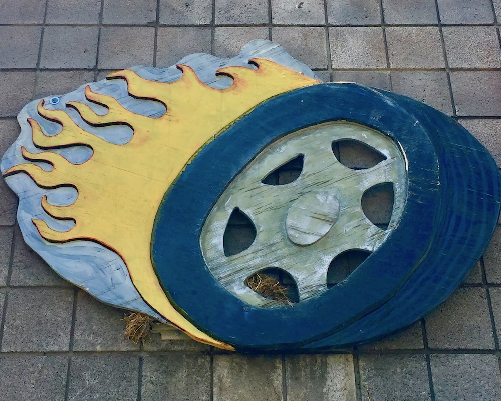 handmade artwork of car wheel with fire attached to masonry wall