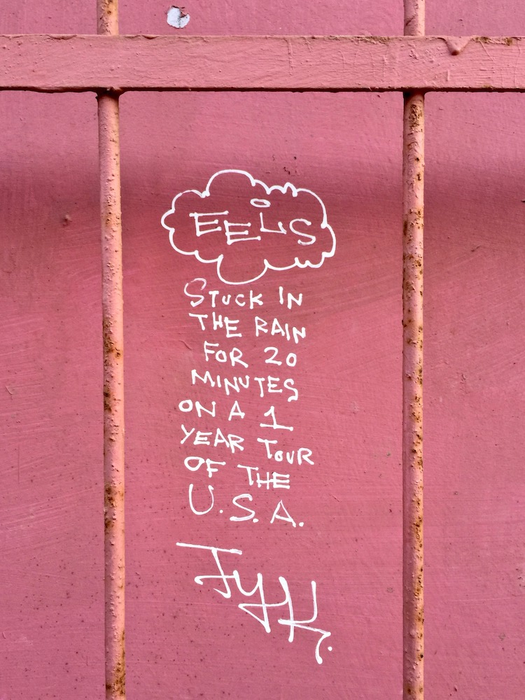graffiti on pink wall reading "Stuck in the rain for 20 minutes on a 1 year tour of the USA"