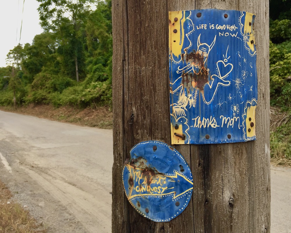 paintings made from flattened tin cans nailed to a utility pole