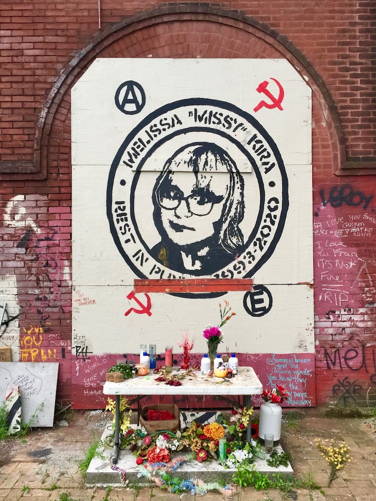 memorial portrait painted on brick wall with candles and flowers below