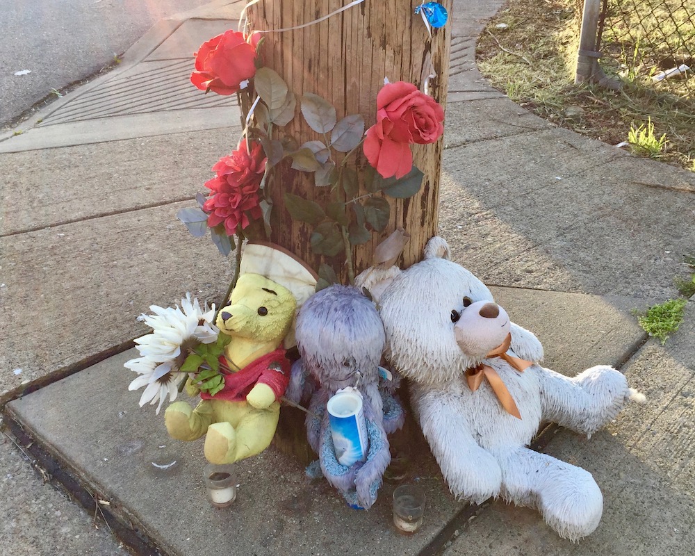 roadside memorial including stuffed animals, candles, and plastic flowers
