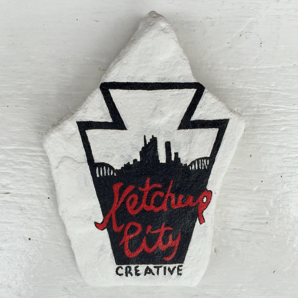 stone hand painted with logo for Ketchup City Creative including silhouette of the Pittsburgh skyline