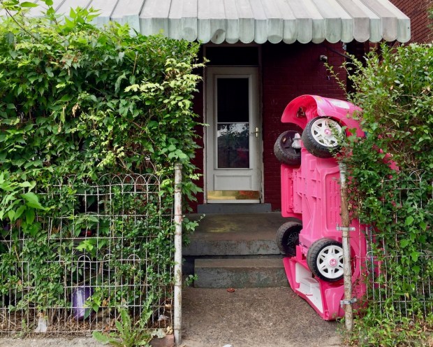 large pink toy car parked vertically in front of brick house