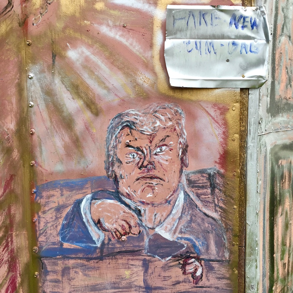 painting of Donald Trump on metal shed with sign reading "Fake news scum-bag"