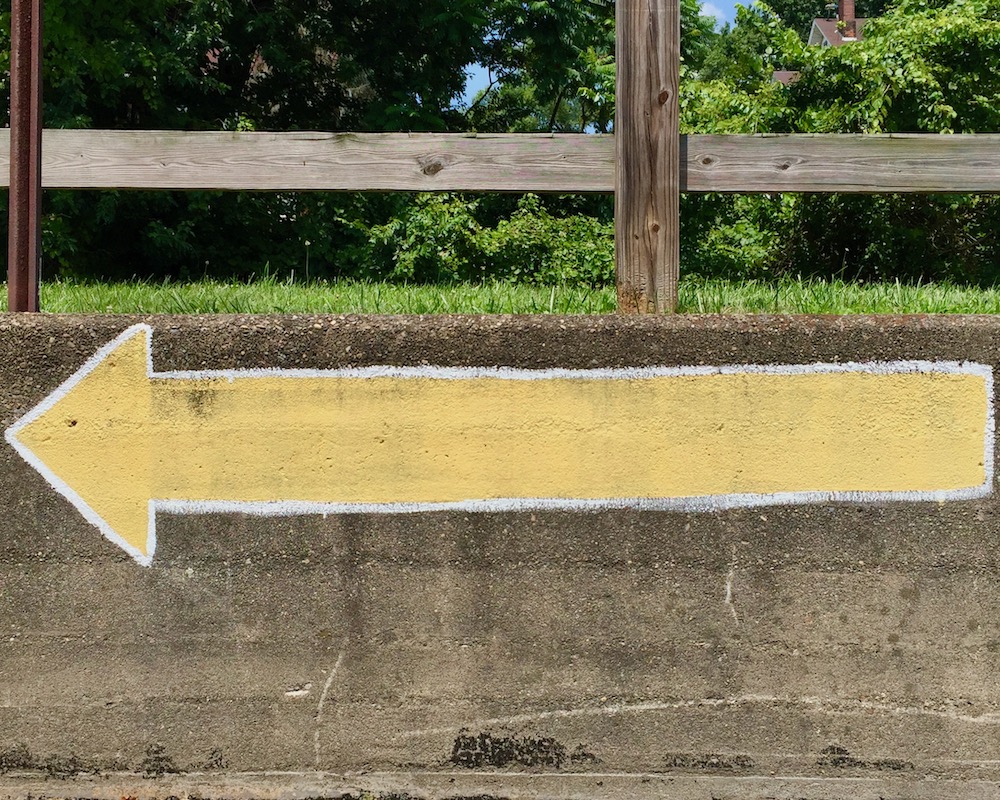 long yellow arrow painted on masonry wall