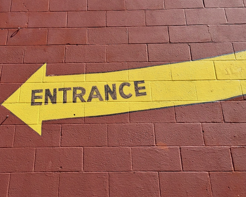 yellow arrow with word "Entrance" painted on it on cinderblock wall