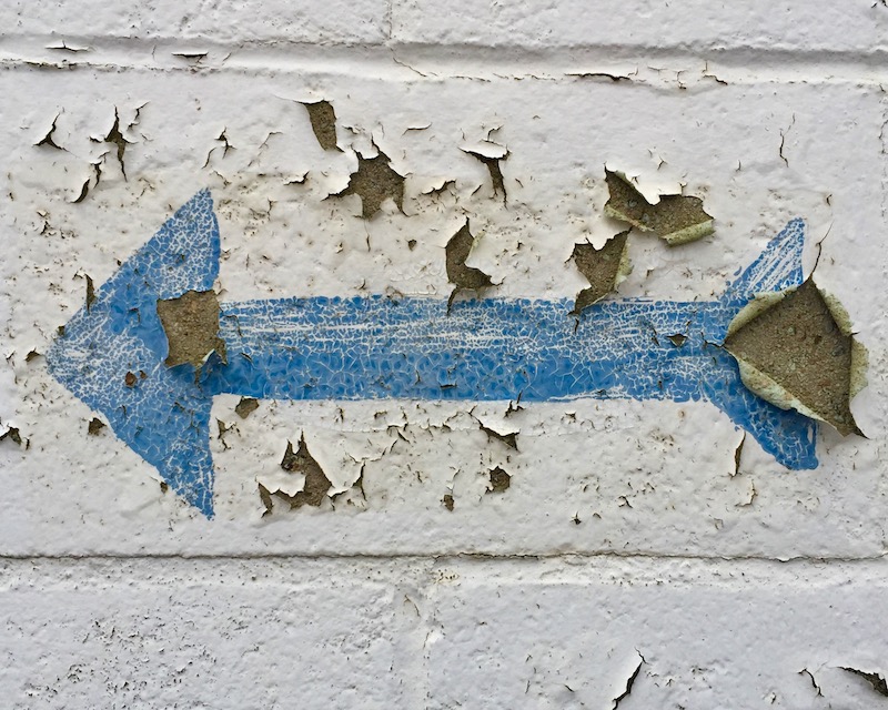 blue arrow painted on peeling cinderblock wall
