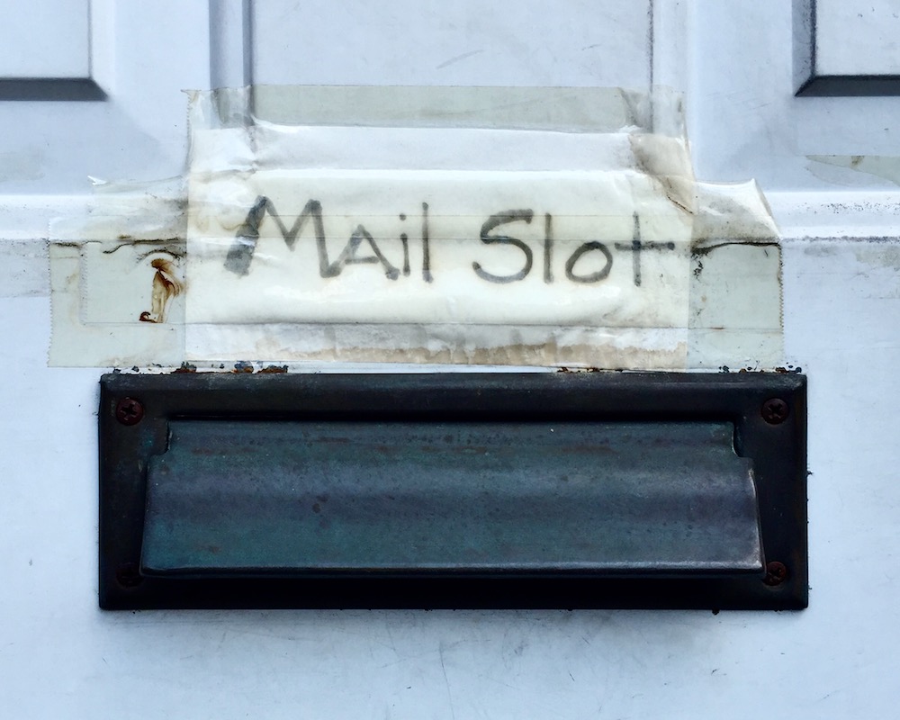 handwritten sign reading "Mail Slot" taped above mail slot in front door