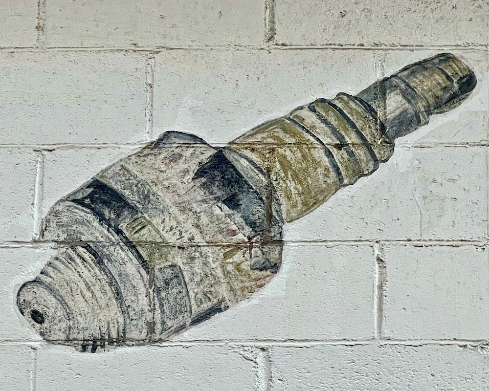 painting of large spark plug on cinderblock wall