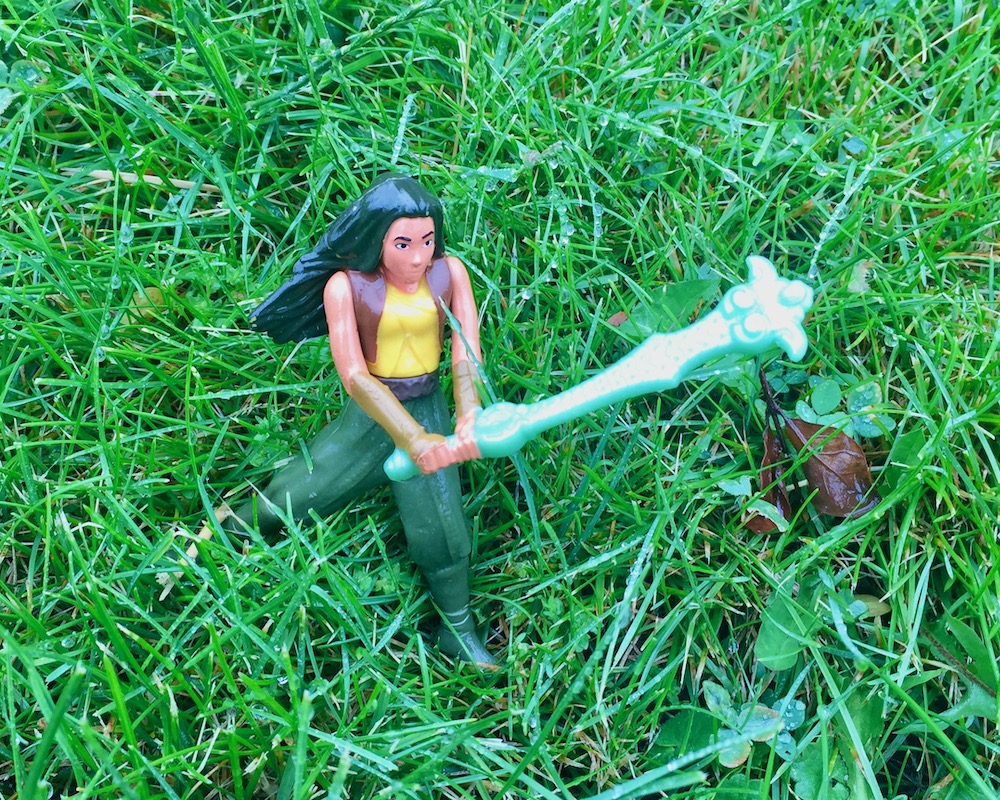 doll with large weapon in tall grass