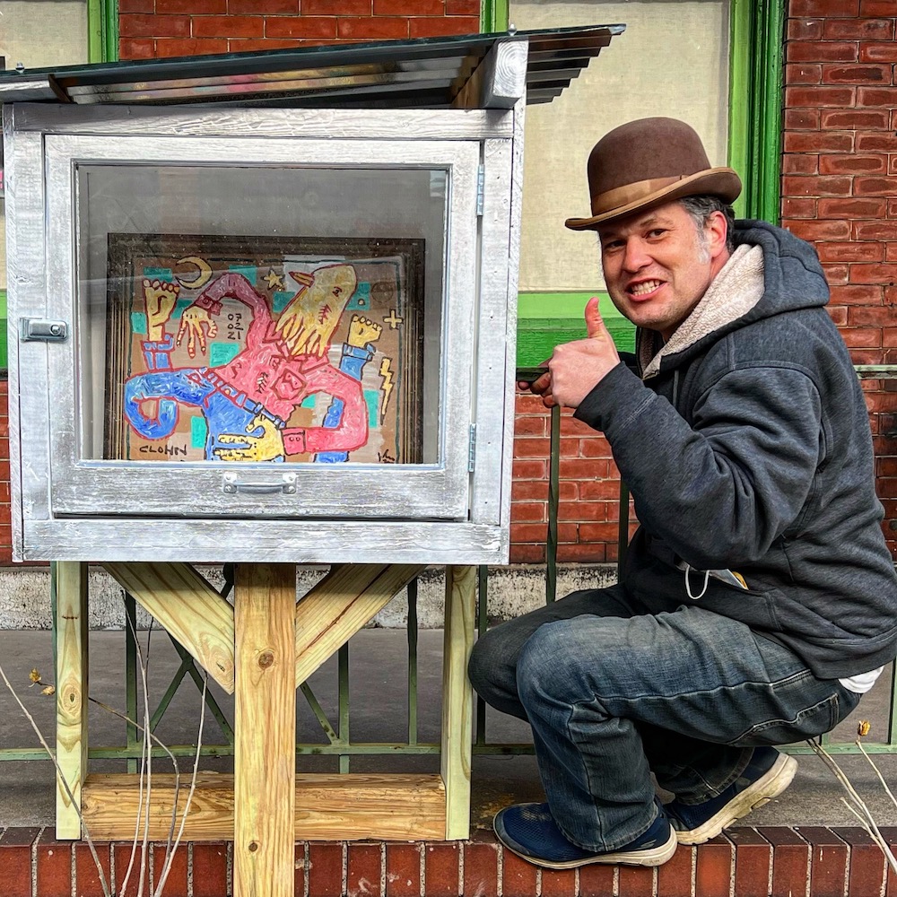 Artist John Lee with his art inside little free art gallery