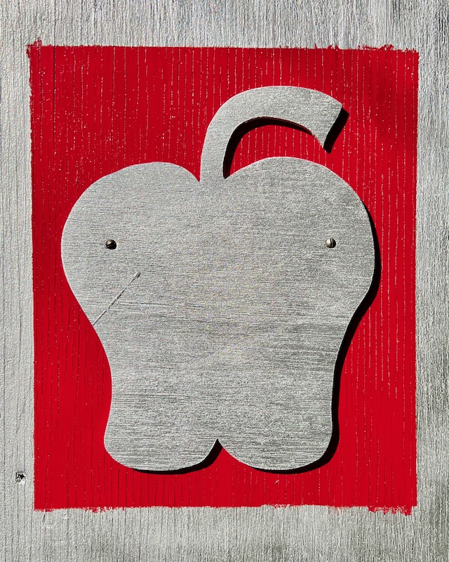 side panel of little free art gallery featuring a cut out silver apple on a red background