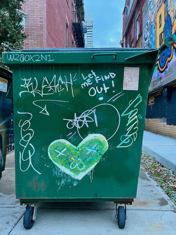 wheatpaste street art on dumpster of heart-shaped face with Xs over eyes
